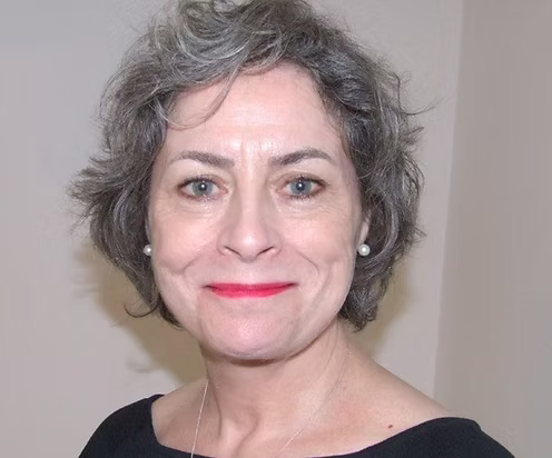 Woman with gray hair and red lipstick smiling against a plain background