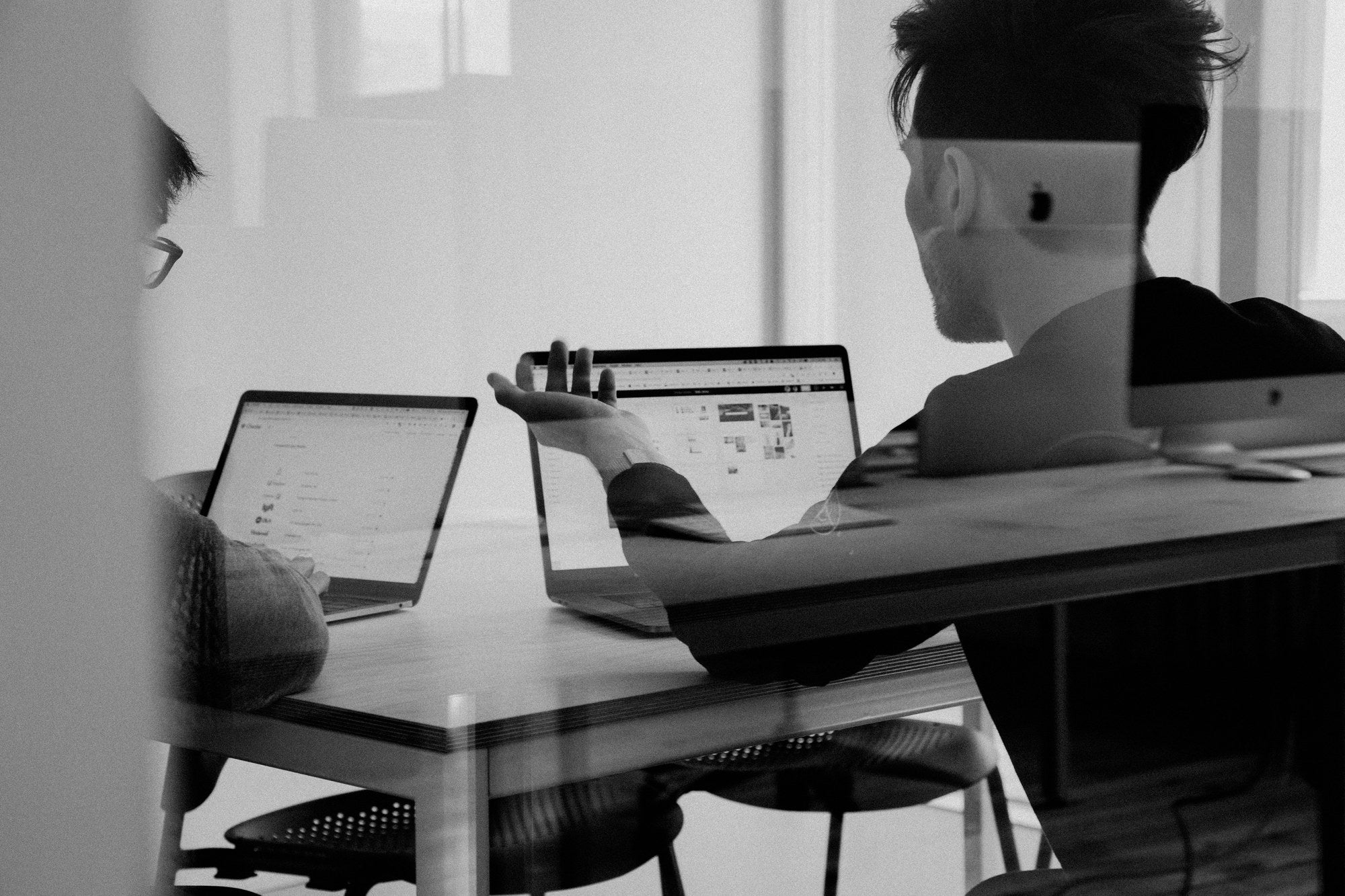 Two professionals reviewing business case documents on laptops in a collaborative workspace, representing Treasury Green Book business case writing and review