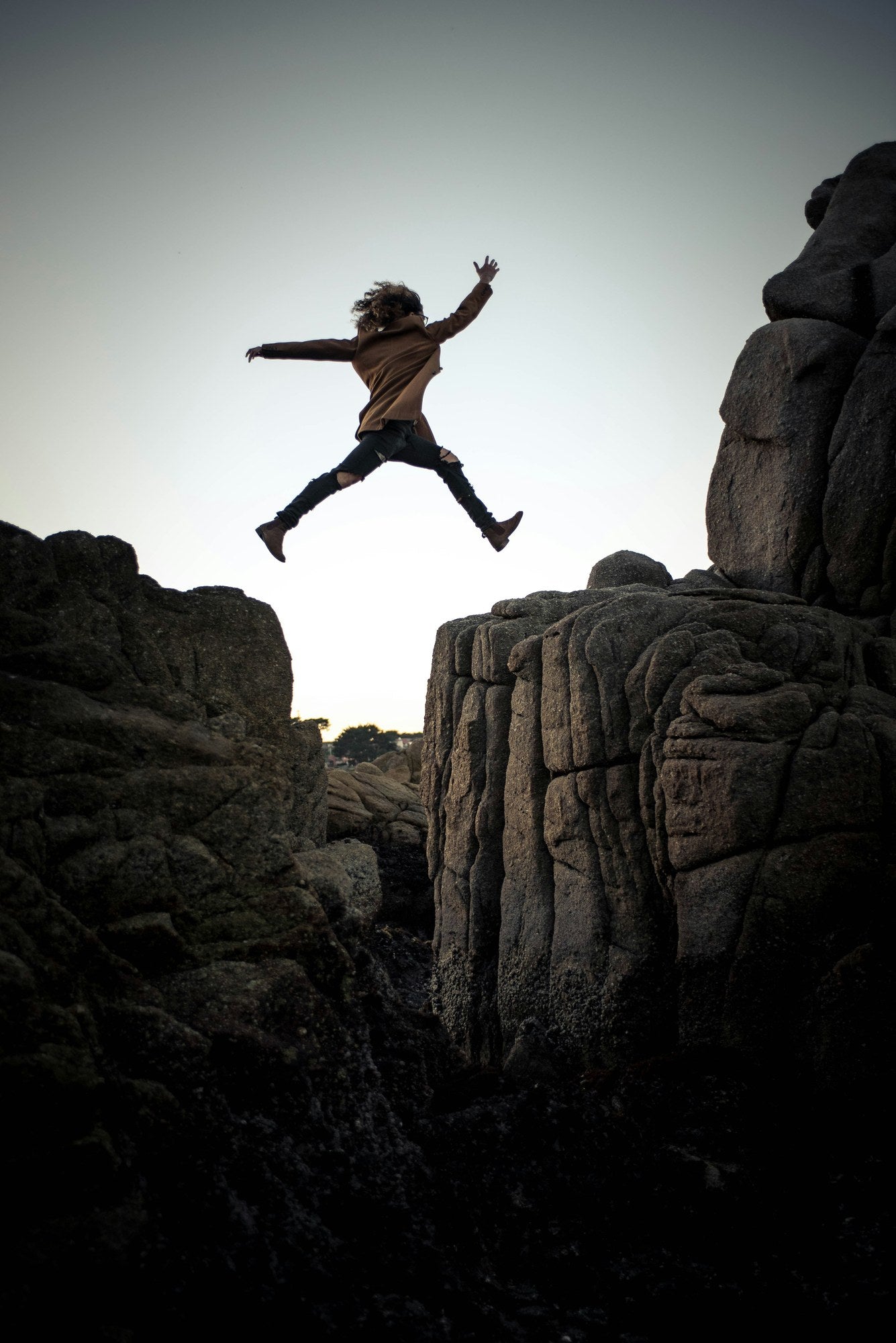 Person leaping boldly between rocky outcrops at dusk against a grey sky, representing the critical step of programme deployment and the importance of a readiness assessment before launch
