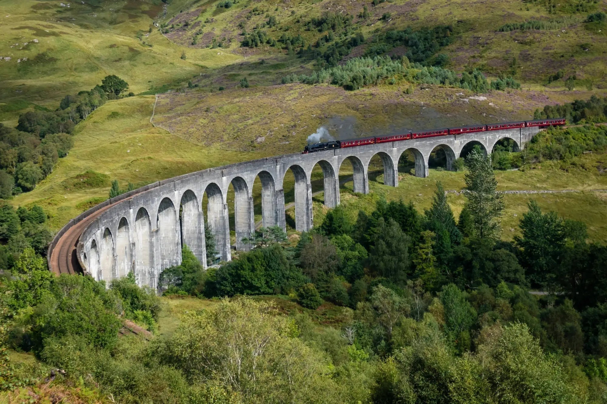 Glenfinnan Viaduct stone bridge with red train crossing