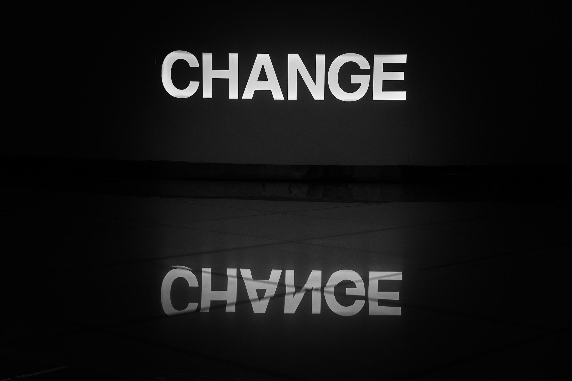 Illuminated CHANGE sign and its mirror reflection against a dark background, representing organisational change management, transformation readiness, and the Able Willing Allowed framework