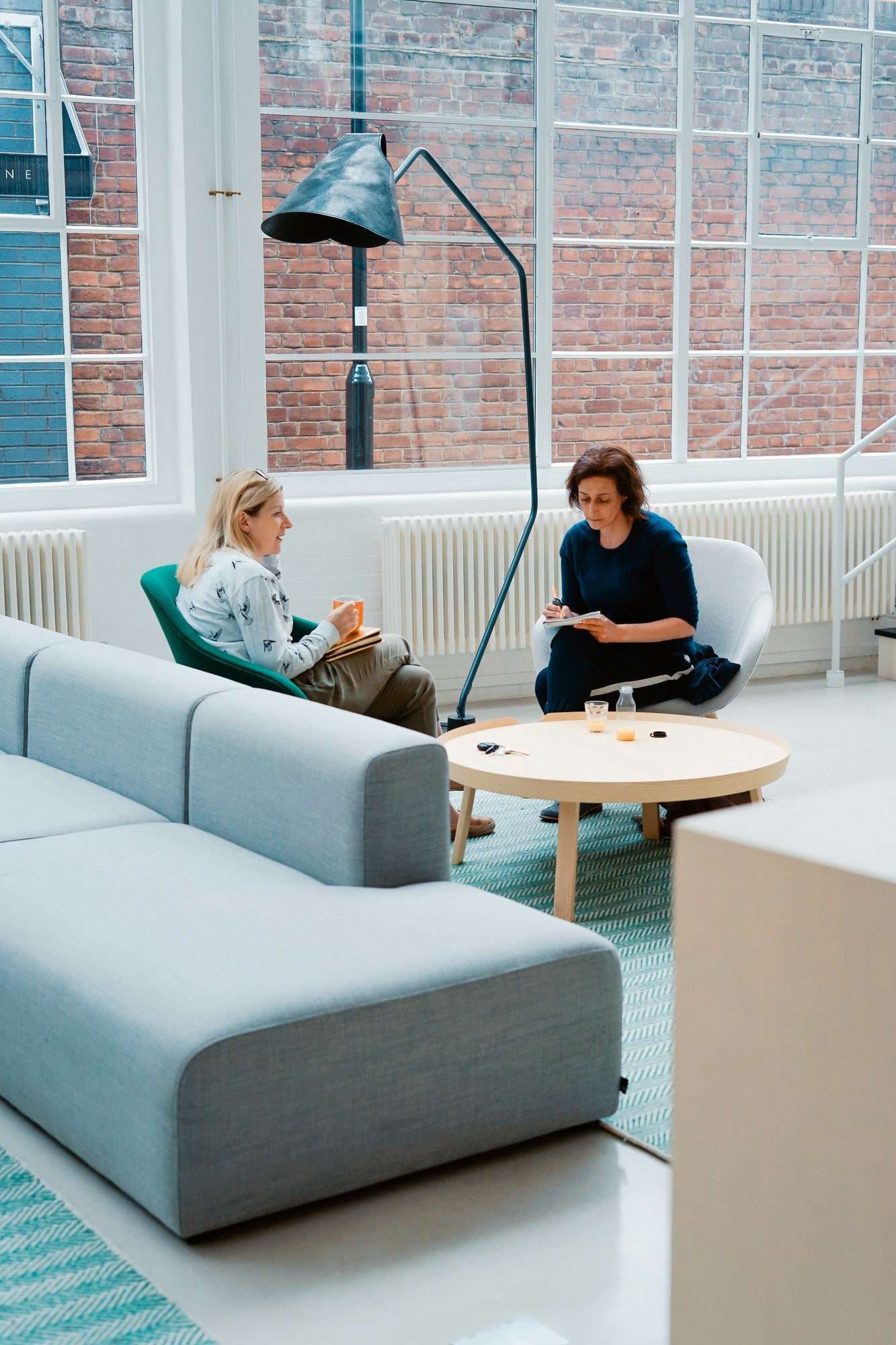 Two professionals in a relaxed coaching conversation in a bright modern workspace, representing executive coaching chemistry and coach-coachee fit assessment
